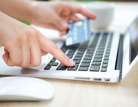 Una persona paga online, tiene su tarjeta de crédito frente al monitor de su computadora. Si eres deudo, te damos varias opciones de pago